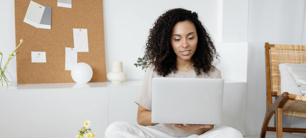 Young woman with curly hair working on her laptop in a cozy home setting, exuding confidence and focus.